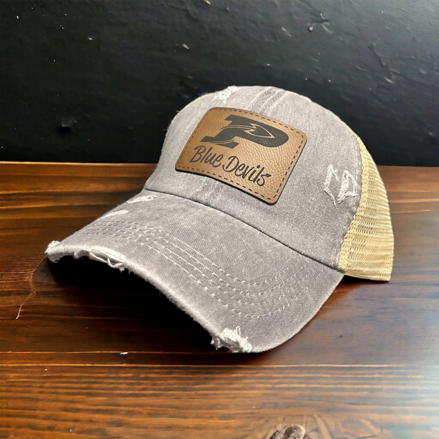 Side angle of a distressed grey ponytail trucker with a brown leatherette Blue Devils patch