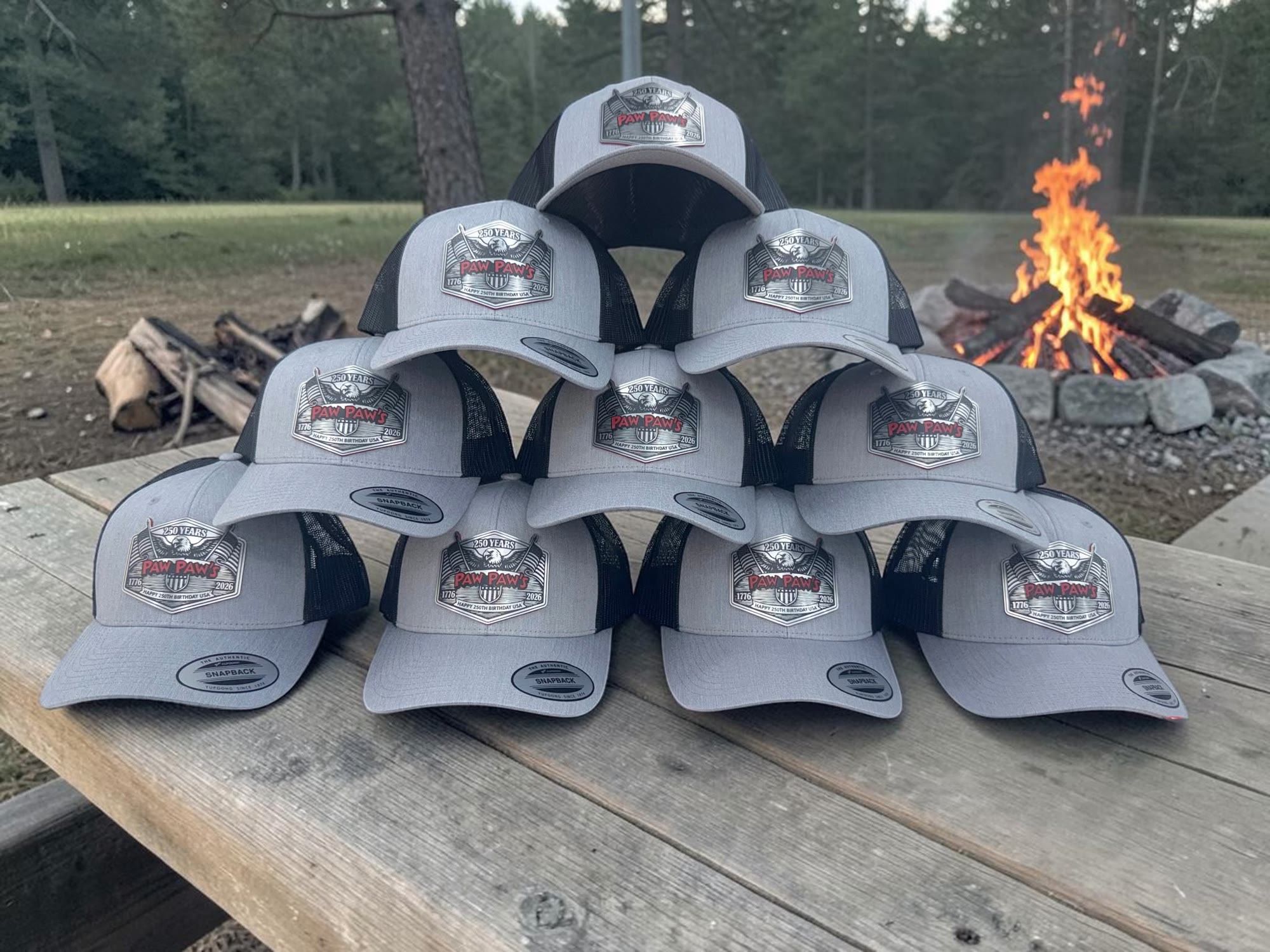 Grey patch hats stacked in a pyramid beside a campfire