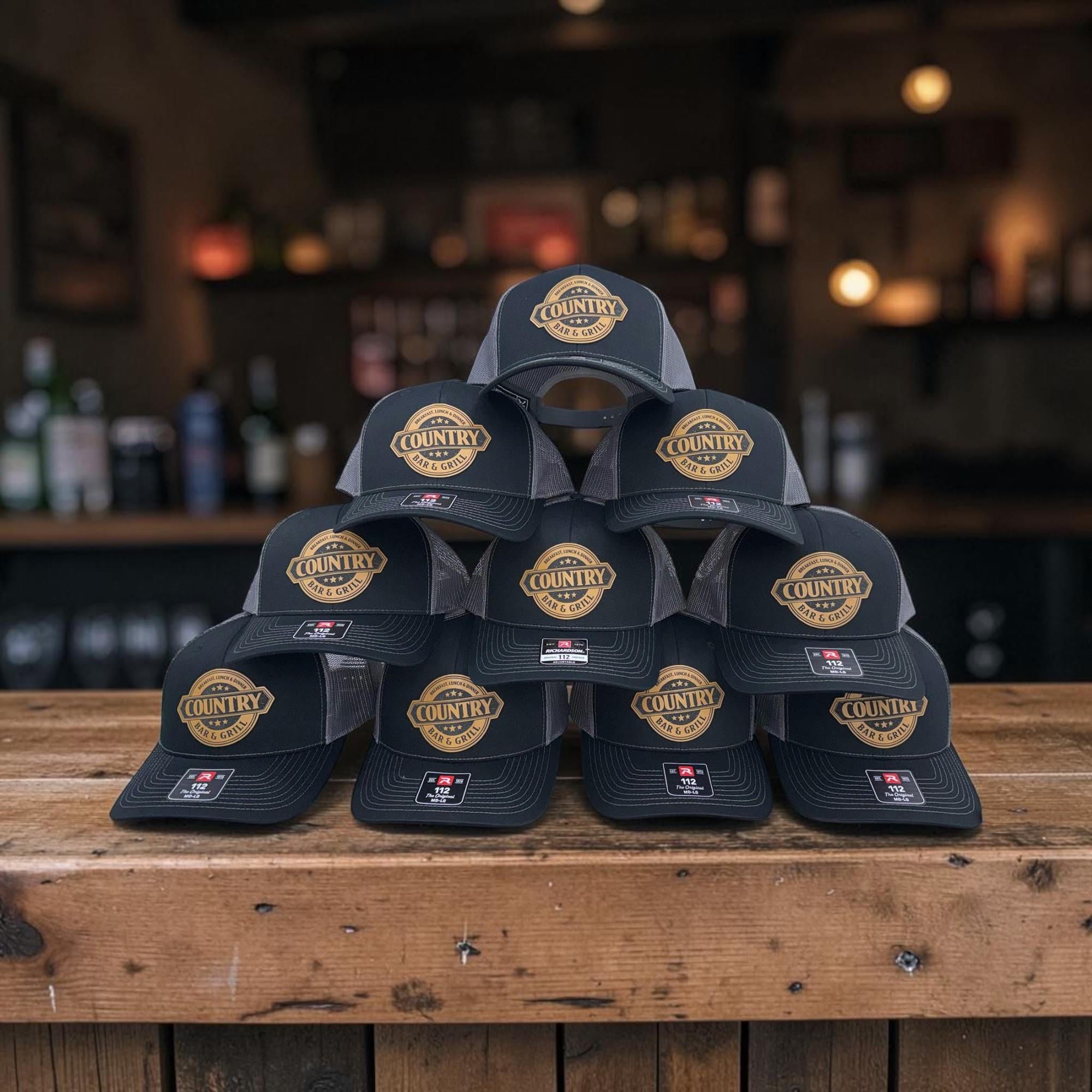 Stack of black Richardson hats with engraved leatherette Country Bar & Grill patches