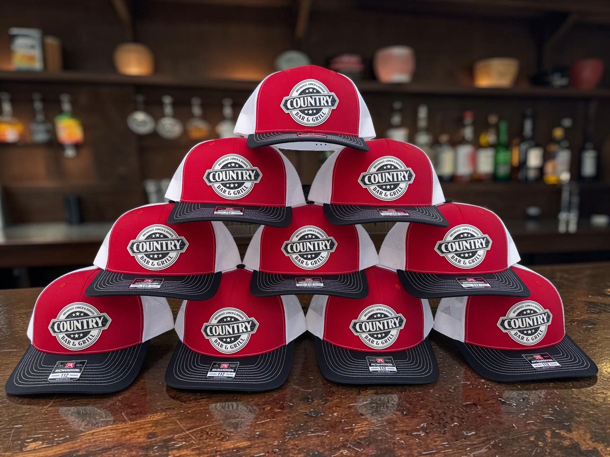 Stack of red Country Bar & Grill patch hats on a bar top