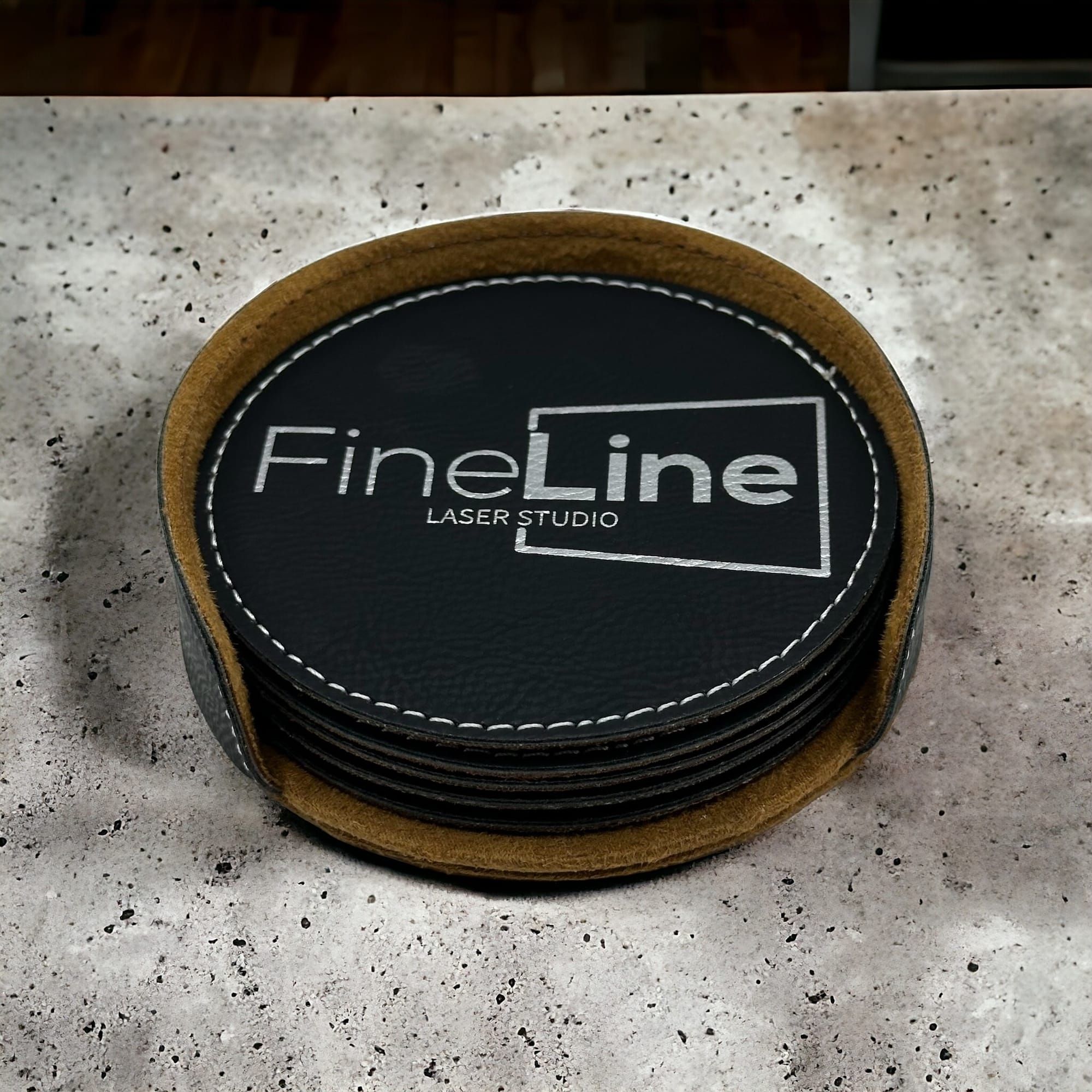 Stack of round black leatherette coasters engraved with the Fine Line Laser Studio logo