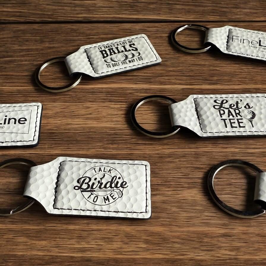 White golf-ball-texture leatherette keychains engraved with golf sayings