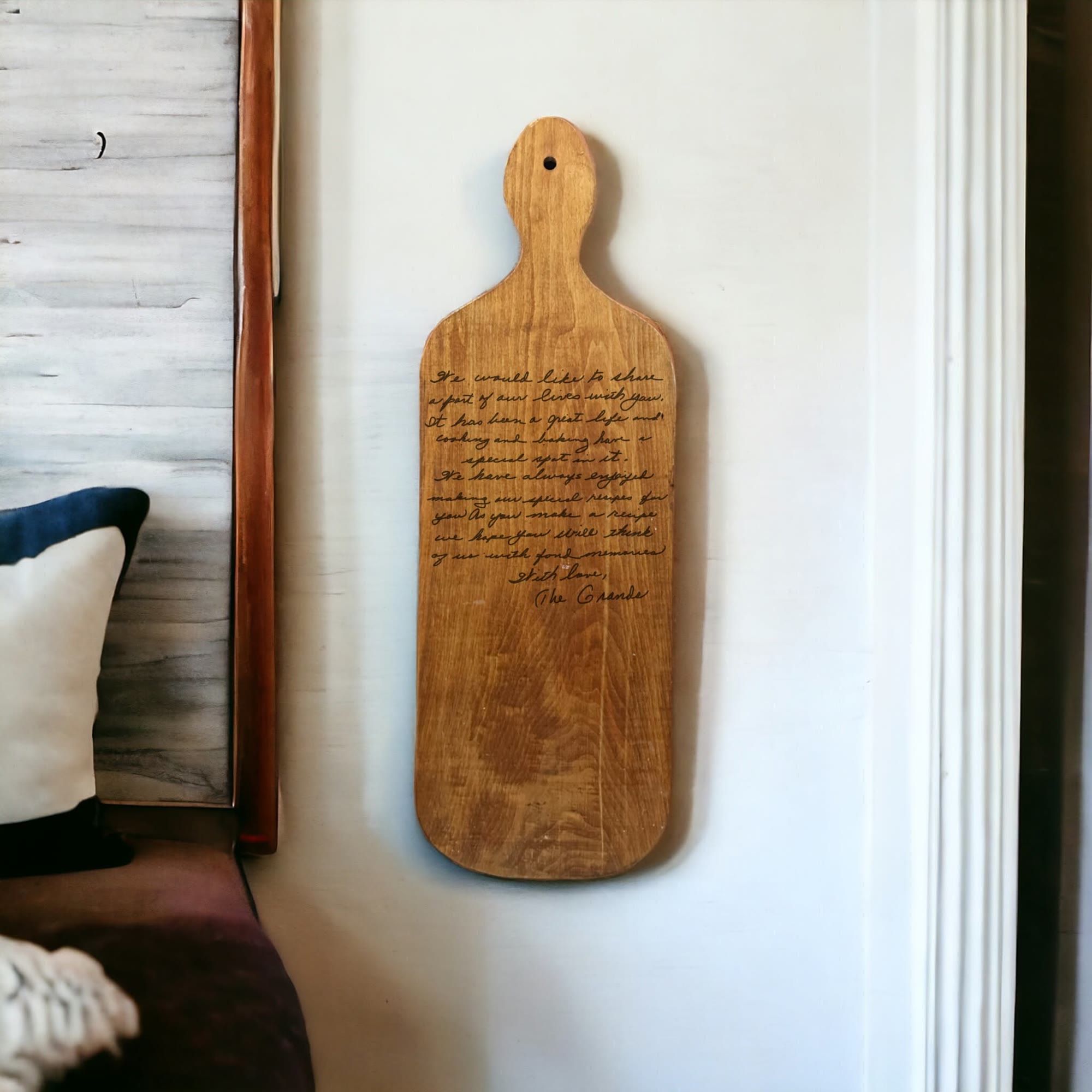 Paddle cutting board engraved with a handwritten family note, hanging on a wall