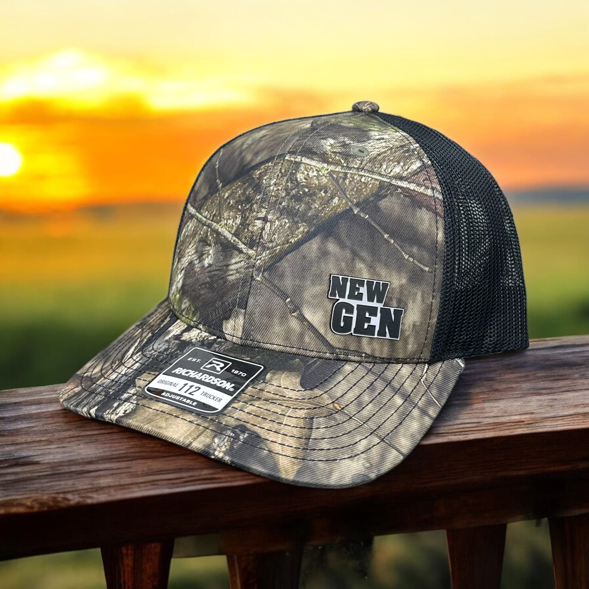 Camo Richardson 112 trucker with a black New Gen patch on a deck rail at sunset